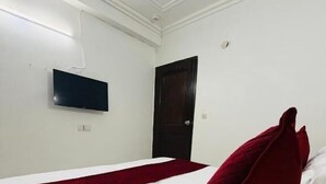 A hotel room with a bed, a flat-screen TV mounted on the wall, and a door. - Hotel RS International (New Delhi)