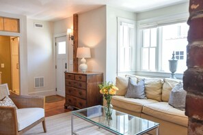 A living room with a glass coffee table, a sofa, a wooden dresser, and a lamp. - Water View, Private Deck and Backyard, Central AC! (Provincetown)