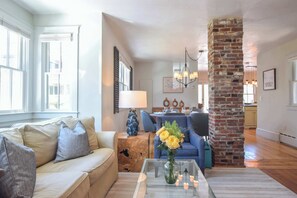 A living room with a sofa, coffee table, and a brick column. - Water View, Private Deck and Backyard, Central AC! (Provincetown)