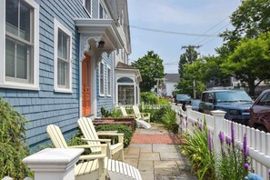 A residential street with blue houses, a white picket fence, and parked cars.