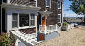 A two-story house with a front porch, a small garden, and a gravel driveway. - Water View, Private Deck and Backyard, Central AC! (Provincetown)