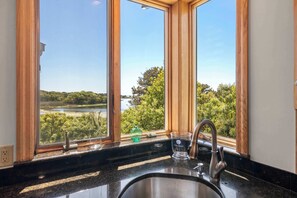 A kitchen with a sink, a window with a view of a lake and trees, and a wooden frame around the window. - Waterfront Escape, Game Room, Dog Friendly! (Chatham)
