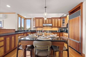 A modern kitchen with wooden cabinets, a central island with seating, and a hanging light fixture. - Waterfront Escape, Game Room, Dog Friendly! (Chatham)