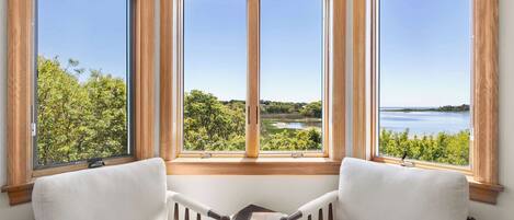A corner room with a large bay window overlooking a lake and greenery.