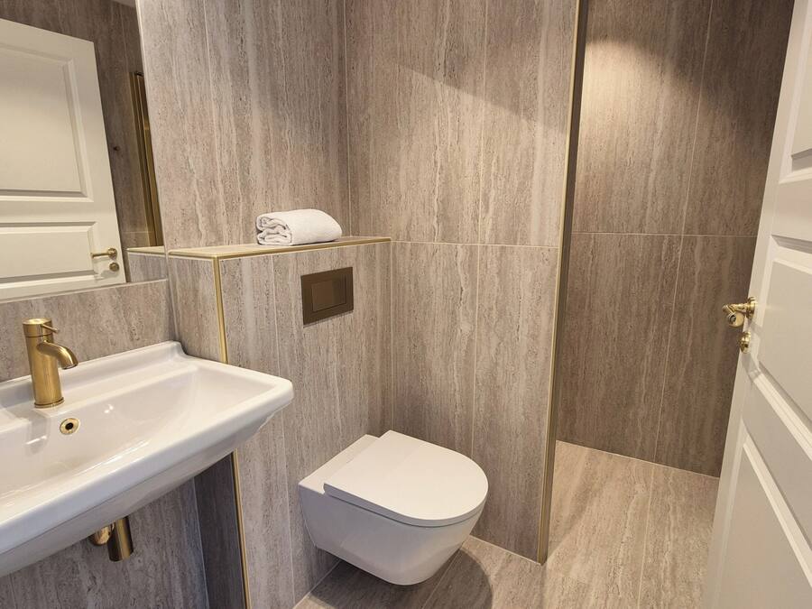 A bathroom with a white sink, gold faucet, and a toilet.