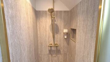 Een douche met een gouden douchekop en slang, een klein spiegel en een zeepdispenser aan de muur.