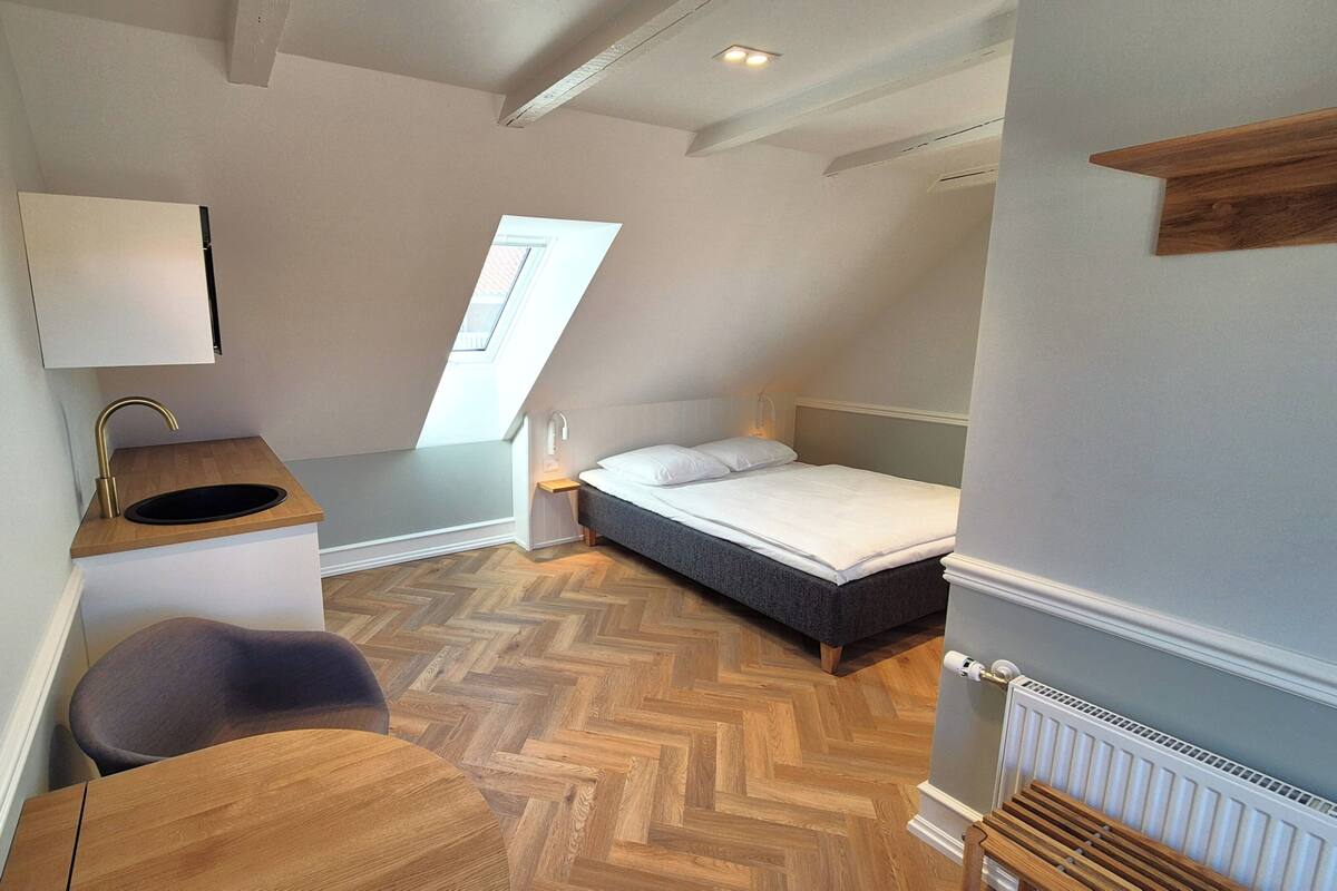 Habitació petita i moderna amb un llit, una taula de treball i una finestra.