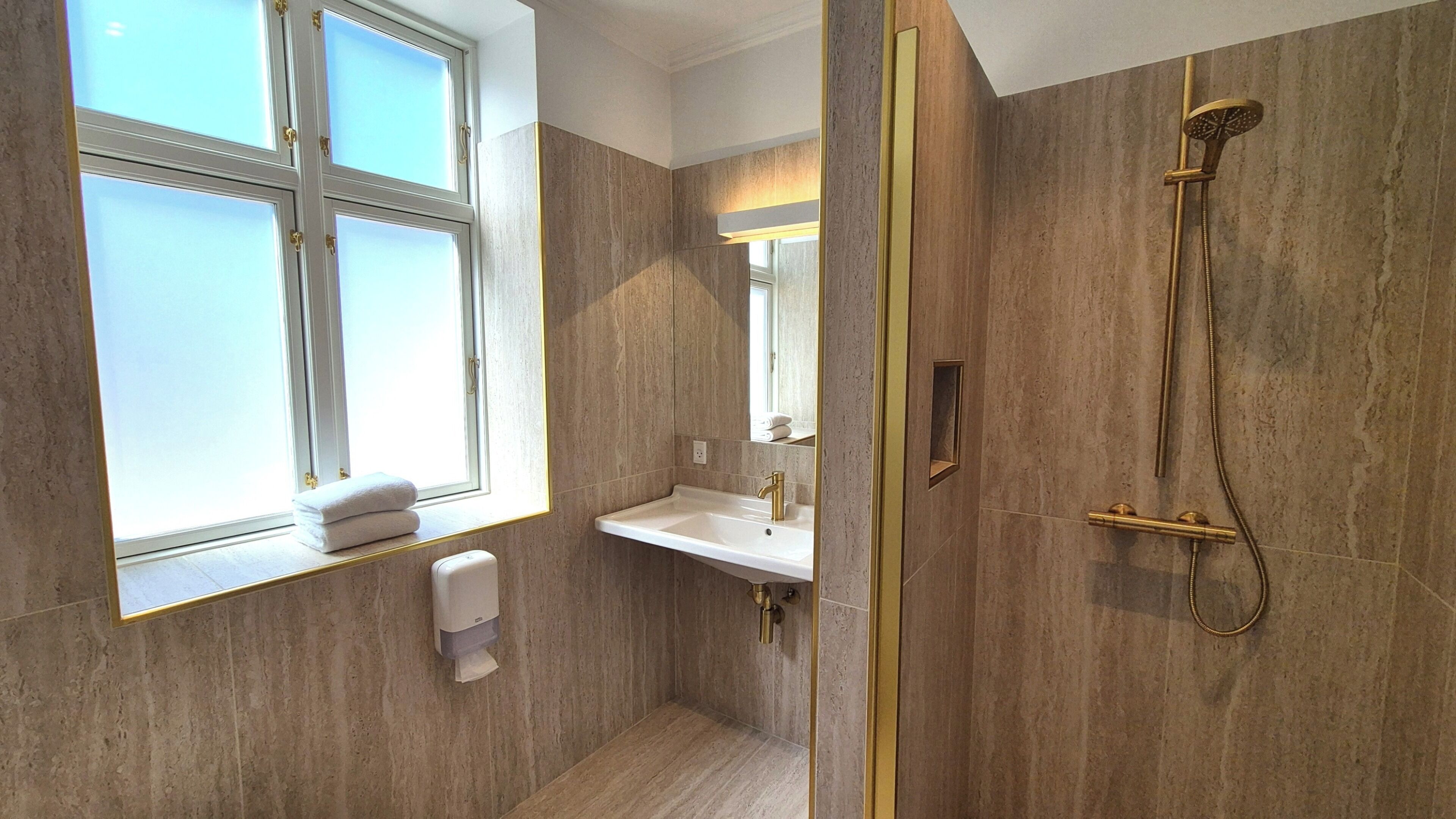 A bathroom with a window, a sink, a mirror, and a shower.