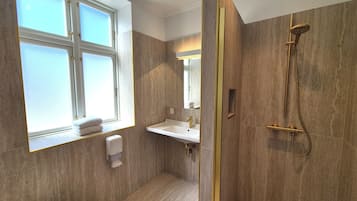 A bathroom with a window, a sink, a mirror, and a shower.