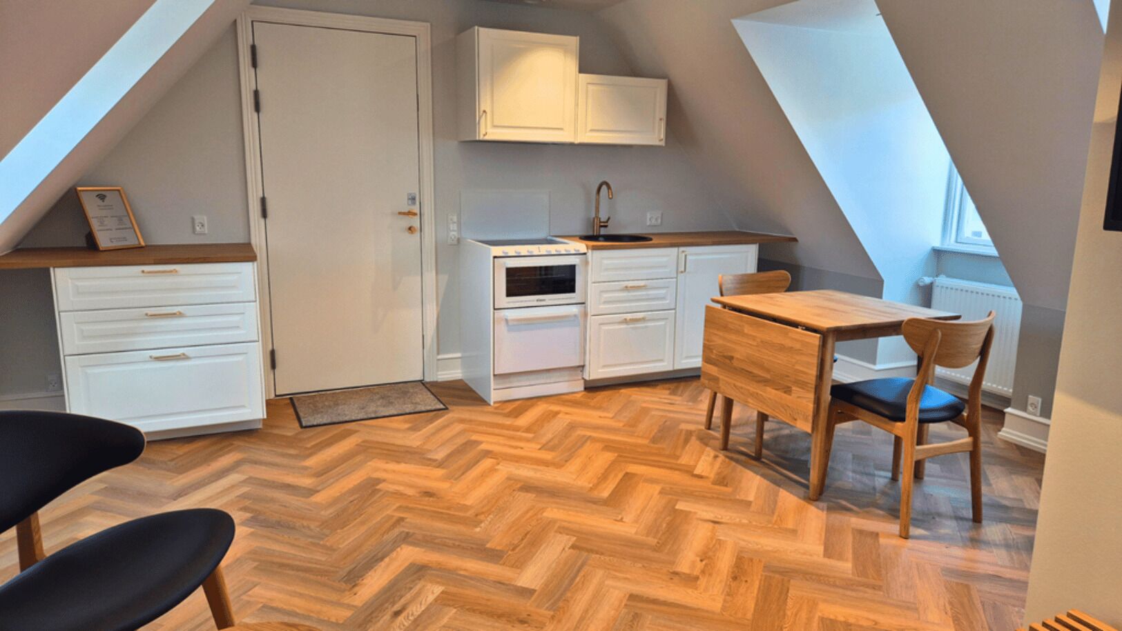 Una cocina con armarios blancos, una mesa de comedor de madera y un suelo con diseño de espiga.