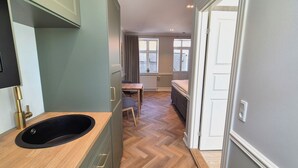 A modern room with a wooden herringbone floor, a small dining table, a sofa, and a built-in sink. - Jacobs Hotel (Ringkøbing)