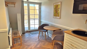 A small kitchenette with a sink, a chair, a table, and a door leading to a balcony. - Jacobs Hotel (Ringkøbing)