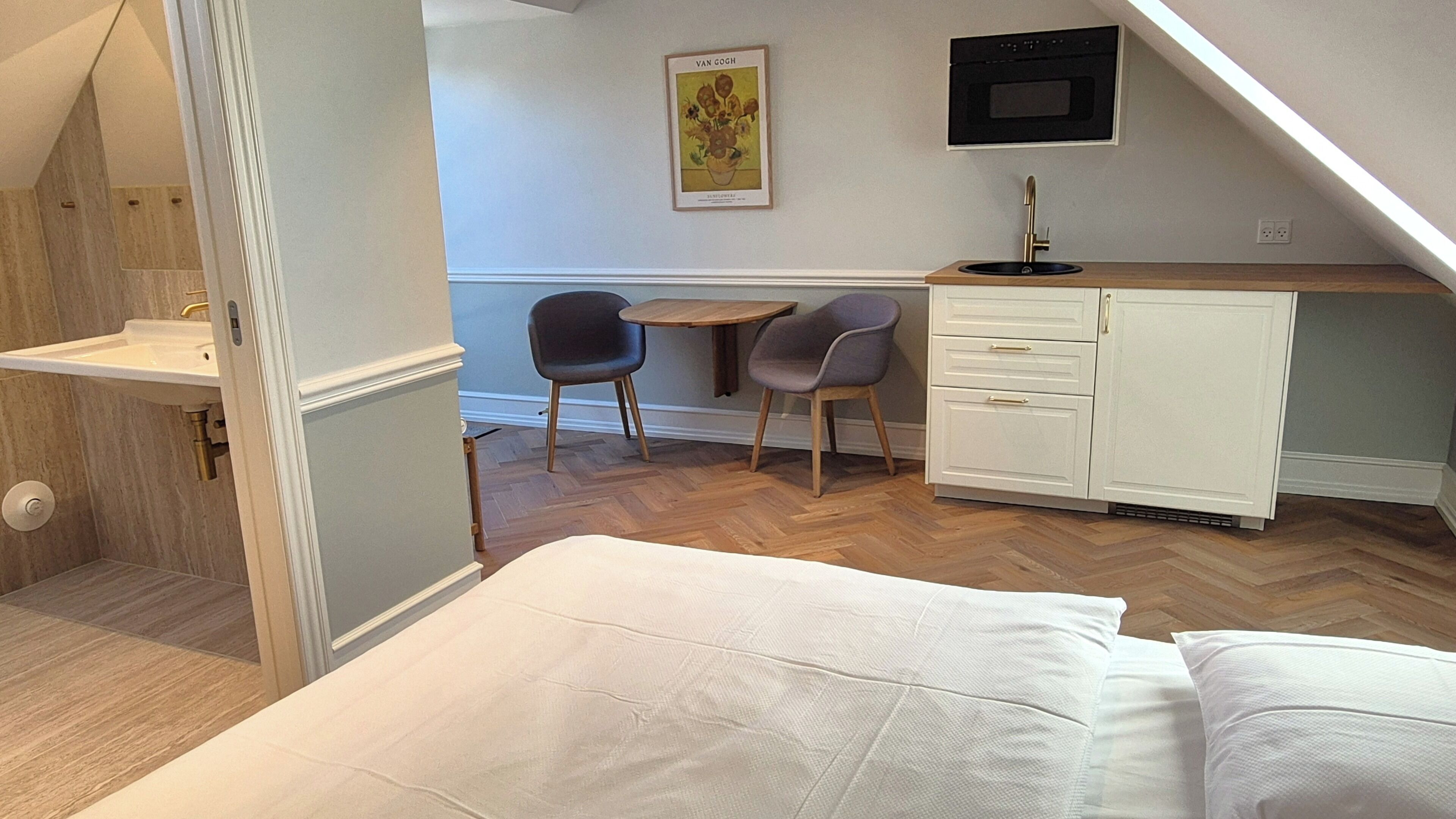 Une chambre à coucher comprenant un lit, un bureau avec deux chaises, un petit meuble et un four fixé au mur.