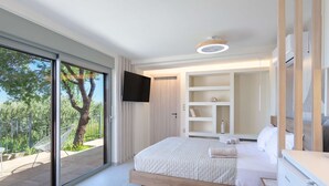 A modern bedroom with a large sliding glass door, a bed with a wooden frame, a built-in TV, and a white wardrobe. - Assini Estate - Pet Friendly Studio With Pool (Pylos-Nestoras)