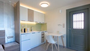 A compact kitchen with white cabinets, a dining table with chairs, a coffee maker, and a door with a metal grille. - Assini Estate - Pet Friendly Studio With Pool (Pylos-Nestoras)