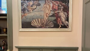 Una stanza con un grande dipinto classico, un armadietto verde e un televisore su uno scaffale.