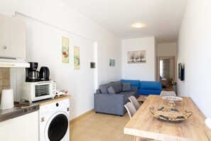 Un espacio habitable compacto con kitchenette, un sofá, una mesa de comedor y una lavadora.