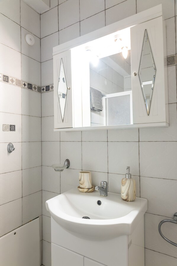 A bathroom with white tiles, a white sink, a mirror with diamond-shaped frames, and a towel rack.