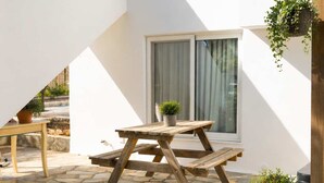 Eine Terrasse mit Holztisch und Bänken, einer weißen Wand und einem Blumenkasten.
