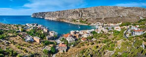 Un village côtier dont les bâtiments sont blottis sur le flanc d’une colline, avec une falaise rocheuse en arrière-plan et une vue dégagée sur la mer.