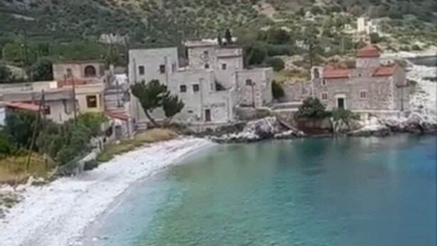 Un village côtier avec des bâtiments en pierre, une plage et une montagne en arrière-plan.