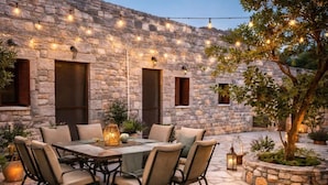 Un espace de restauration en plein air avec des murs en pierre, des guirlandes lumineuses et une table entourée de chaises.
