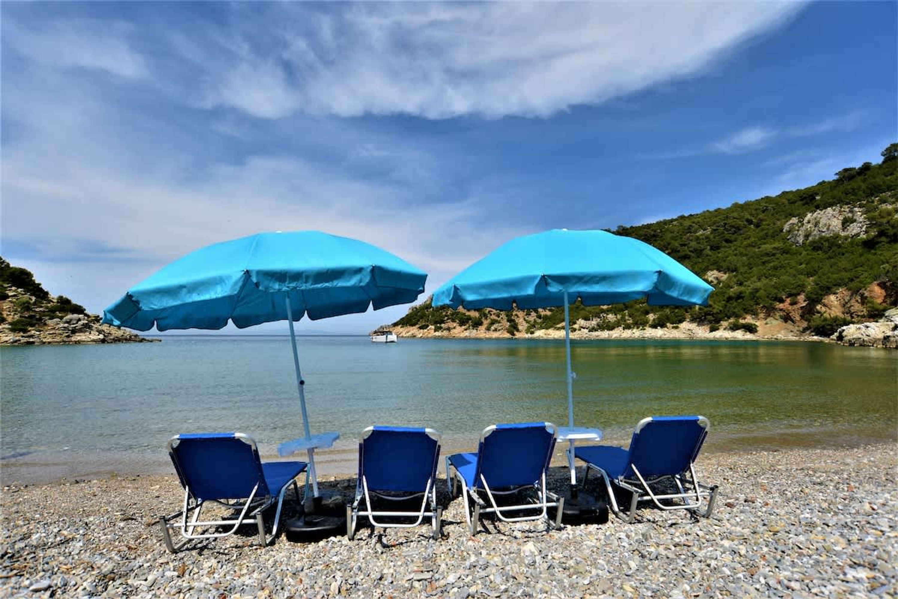 Una playa con cuatro sillas azules para tomar el sol y dos sombrillas azules.