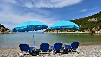 Una playa con cuatro sillas azules para tomar el sol y dos sombrillas azules.