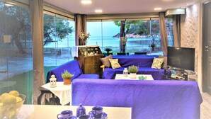 A room with a large window, a sofa, a table with a teapot, and a television. - Private Beachfront House Irene Mare Vagionia Bay (Poros)