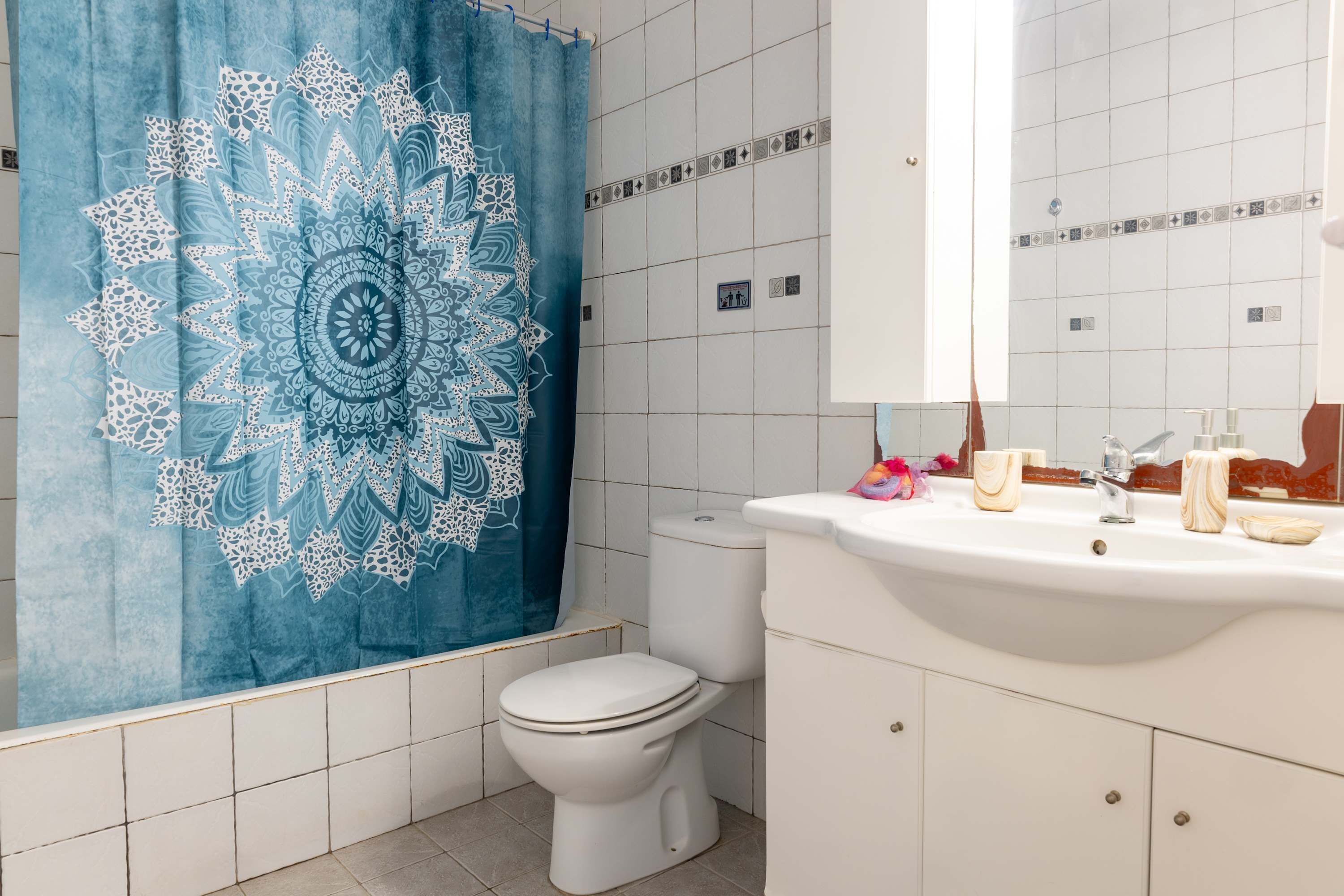 A bathroom with a white toilet, a sink with toiletries, and a blue patterned shower curtain.