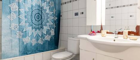 A bathroom with a white toilet, a sink with toiletries, and a blue patterned shower curtain.