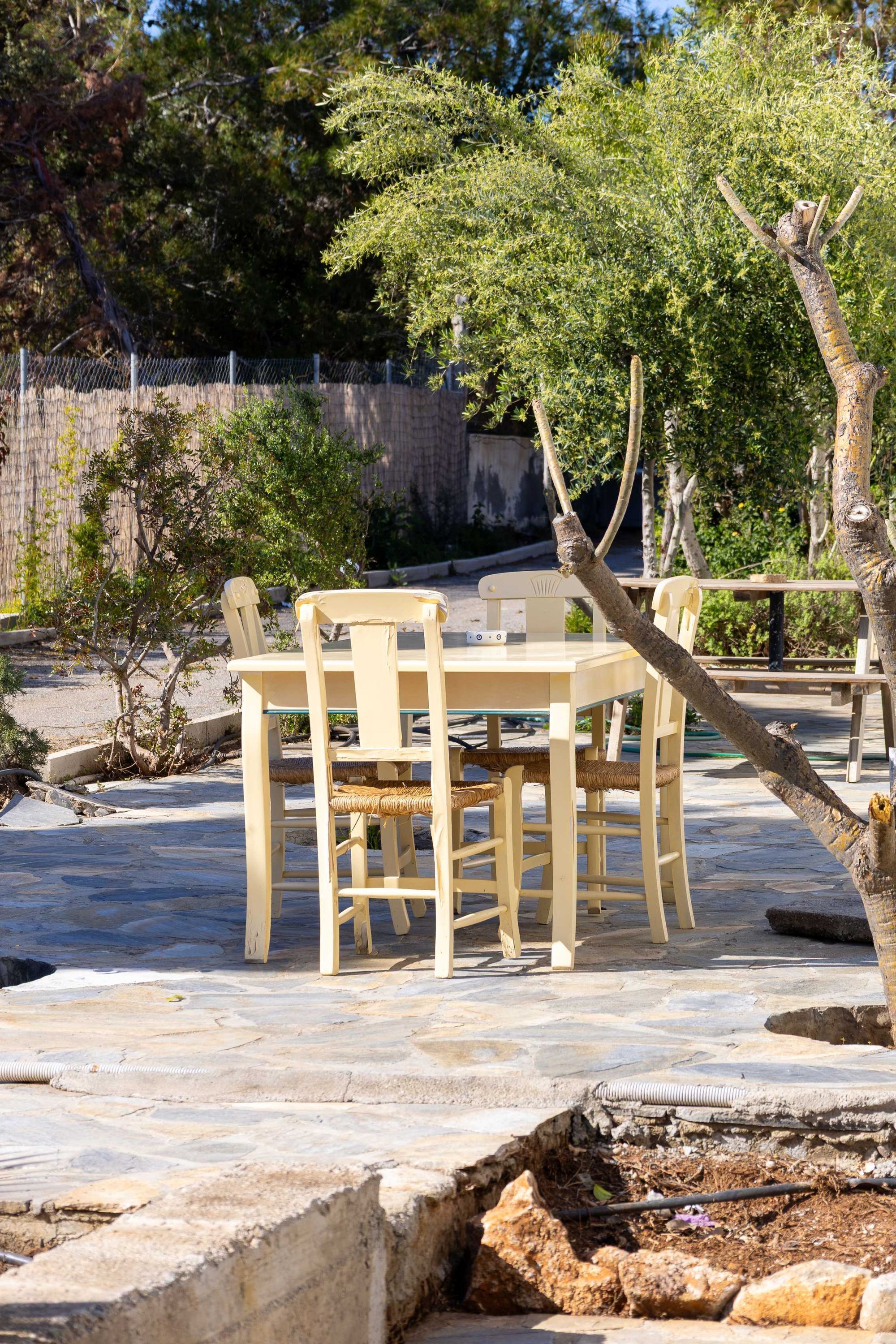 Un área de estar al aire libre con una mesa y sillas, rodeada de árboles y suelo empedrado de piedra.