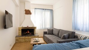 Ein Wohnzimmer mit Kamin, einer Couch, einem Fernseher und einem Fenster mit Vorhängen.