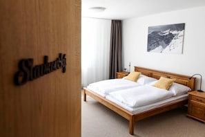 Habitación de hotel con una cama de madera, una mesita de noche, una lámpara, un cuadro en la pared y un cartel en la puerta.