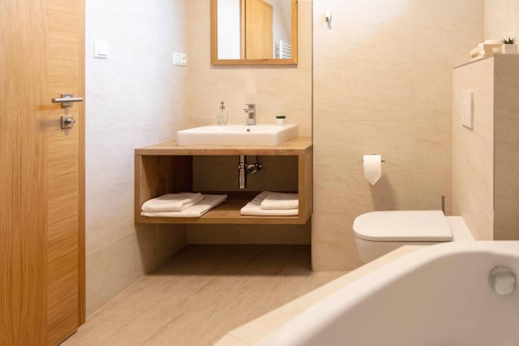 Un baño moderno con tocador de madera, lavamanos blanco, inodoro y bañera.