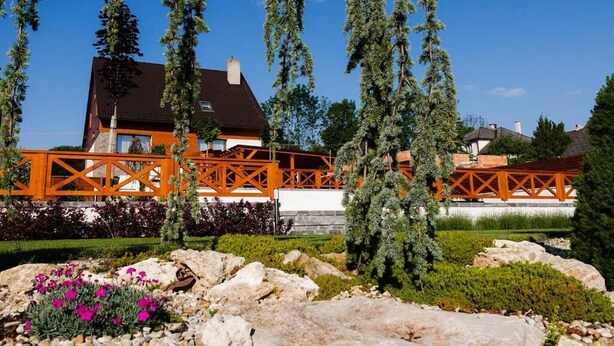 A house with a red wooden deck, surrounded by a garden with rocks and flowering plants. - Chalet Mountain View Nova Lesna (Nová Lesná)