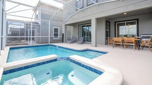 Una piscina amb una estructura de vidre, una zona de pati amb mobles d'exterior i una cuina amb una barbacoa.