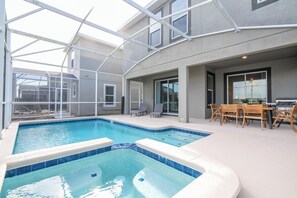 Ein Pool mit Glasumrandung, eine Terrasse mit Gartenmöbeln und ein Küchenbereich mit Grill.