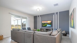 Un saló modern amb un sofà modular, un televisor de pantalla plana fixat a la paret i una finestra gran que ofereix vistes a l'exterior.