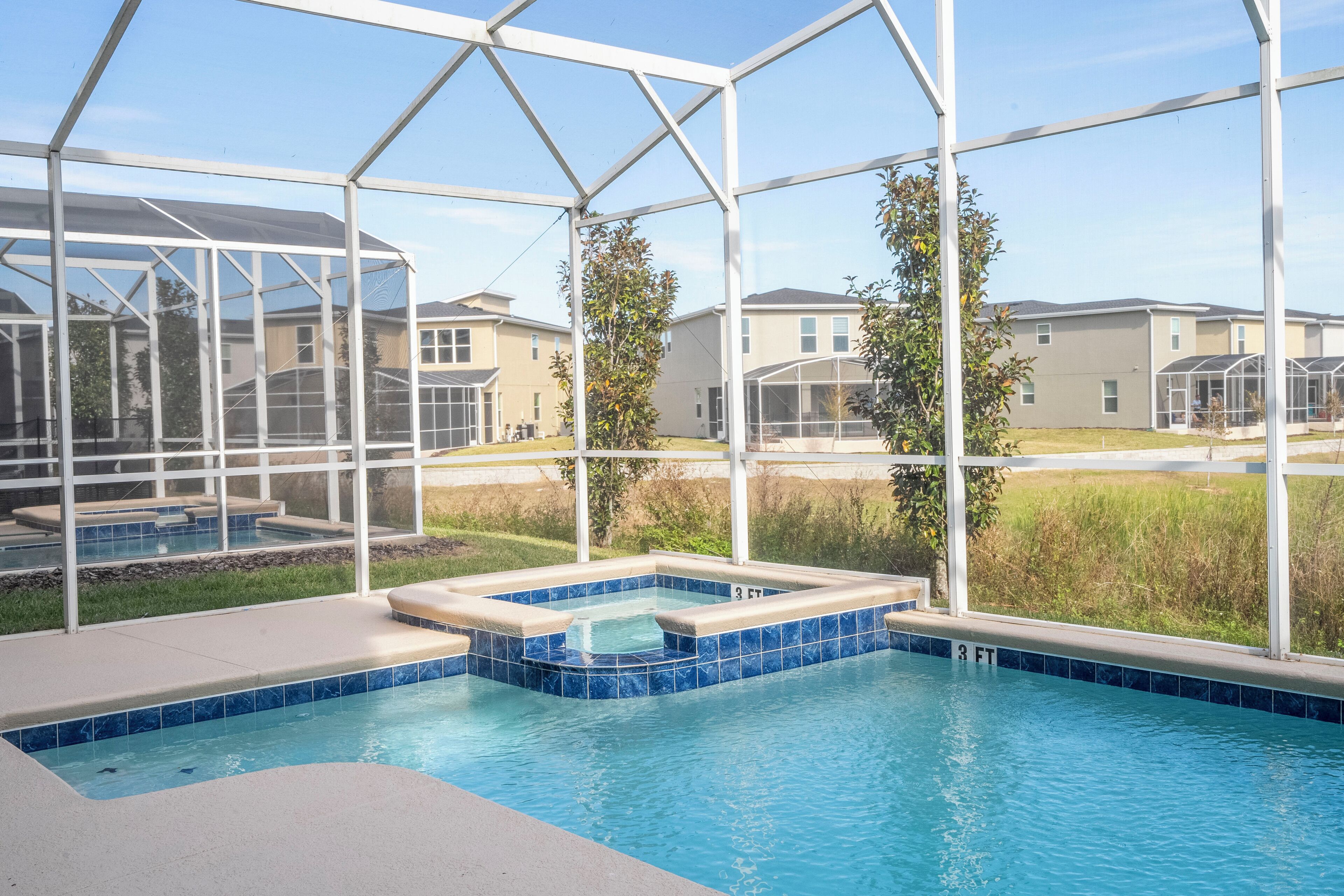 Piscina com banheira de hidromassagem, rodeada por um compartimento de vidro, e edifícios residenciais ao fundo.