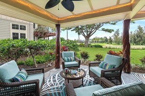 Eine Terrasse im Freien mit Korbmöbeln, einem Deckenventilator und Blick auf einen angelegten Garten.