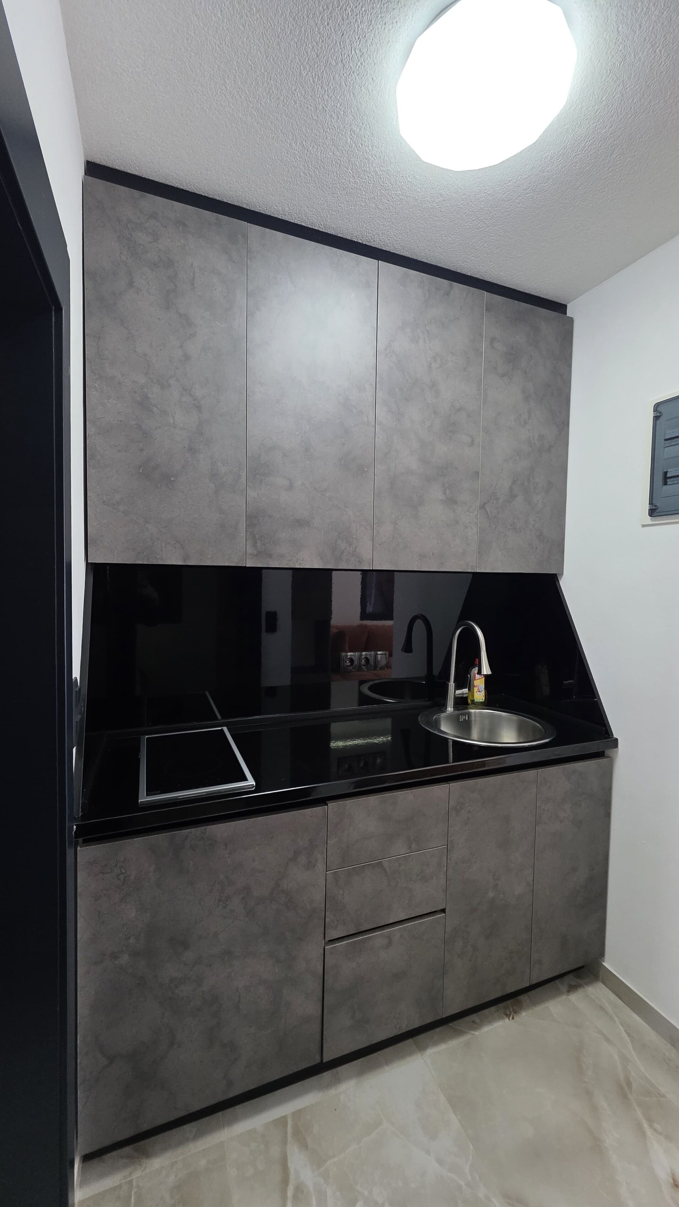 Eine moderne Küche mit schwarzem Arbeitsplatz, grauen Schränken, einer Edelstahl-Spüle und einem eingebauten Backofen.