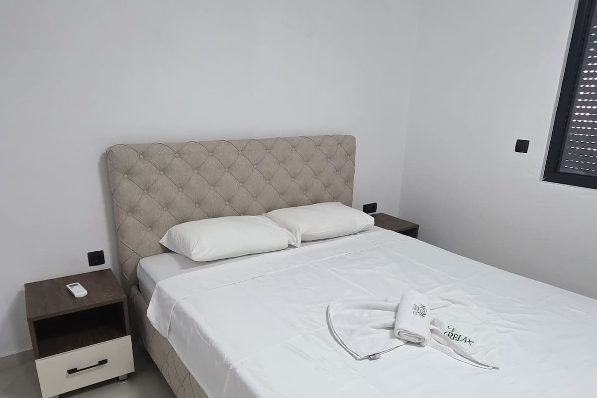 Un lit bien fait, avec une tête de lit, une table de chevet dotée d’un tiroir et un luminaire fixé au mur.