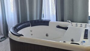 A hot tub in a room with wooden ceiling beams, large windows with sheer curtains, and a tiled floor. - Vile Relax (Ulcinj)