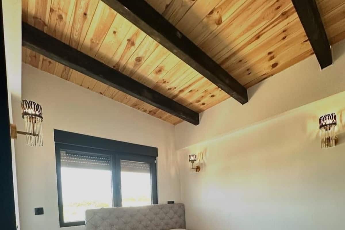 Une chambre à coucher avec un lit, des tables de chevet, une fenêtre et un plafond en bois.