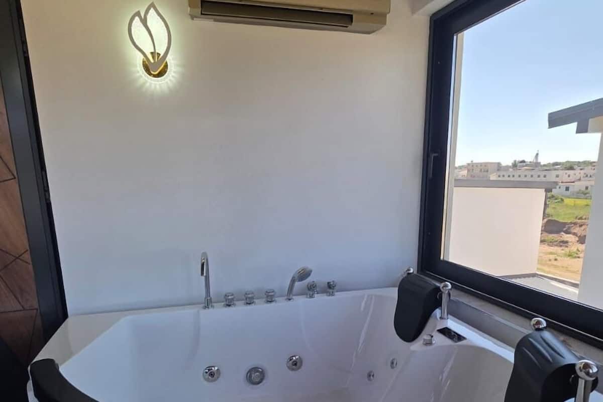Une salle de bain moderne avec une baignoire sur pieds, un climatiseur fixé au mur et une fenêtre donnant sur l’extérieur.