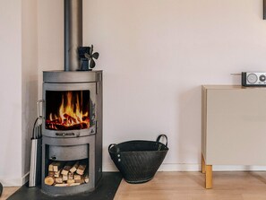 A wood-burning stove with a visible fire, a metal bucket, and a cabinet. - 9 Person Holiday Home in Skagen (Skagen)