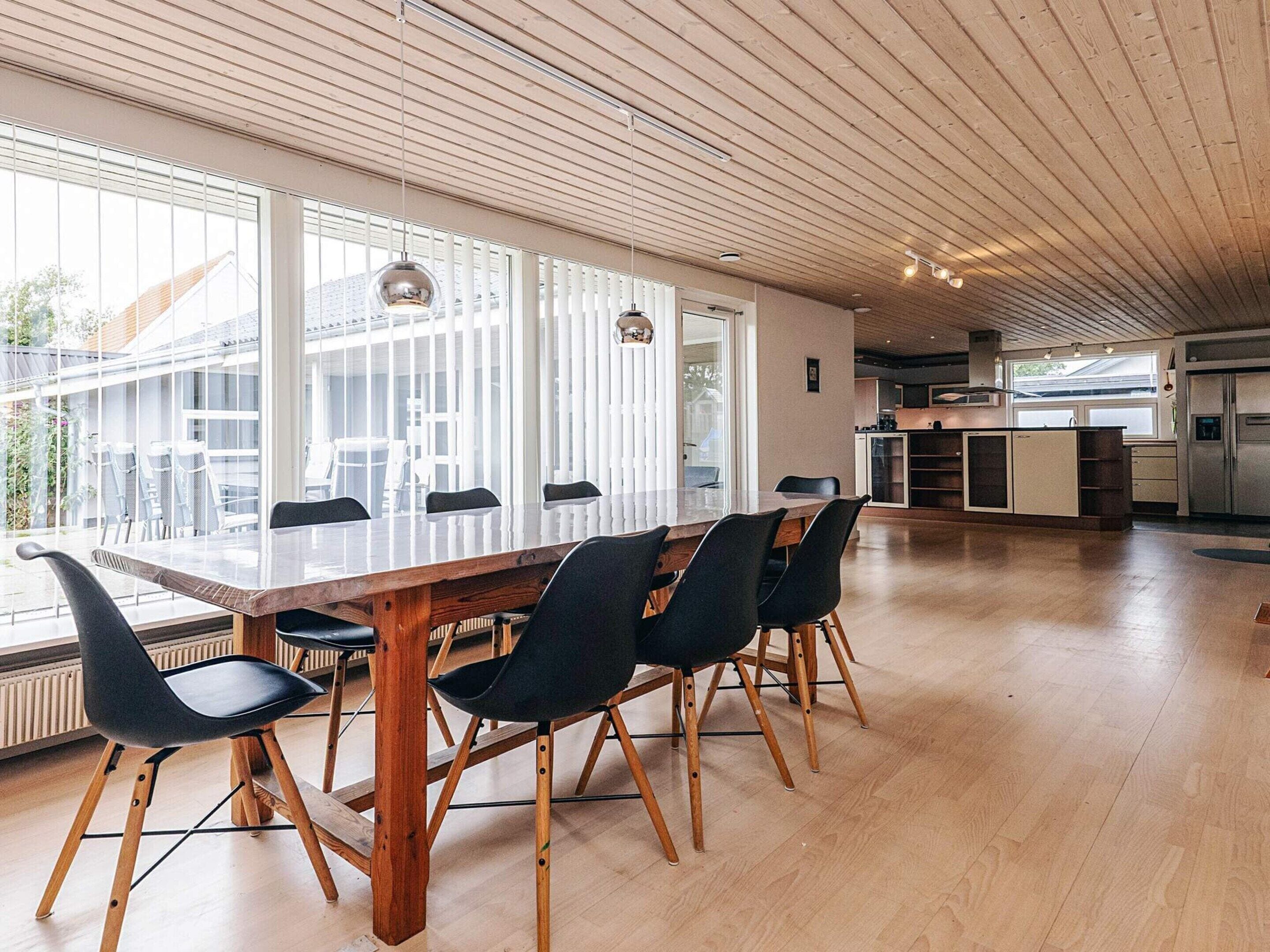 Et rummeligt køkken med træloft, store vinduer og en central ø.