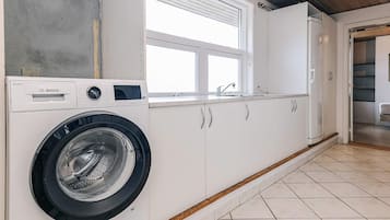 A compact laundry room with a Bosch washing machine, white cabinets, a window, and a wooden ceiling.