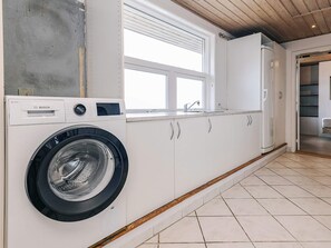 Une petite buanderie équipée d’un lave-linge Bosch, de meubles blancs, d’une fenêtre et d’un plafond en bois.